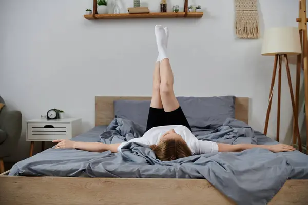 Una giovane donna si sdraia sul suo letto con le gambe in aria, godendo di un momento di relax a casa. — Foto stock