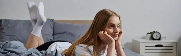 A young woman lays in bed, lost in thought, with her feet up in the air. — Stock Photo