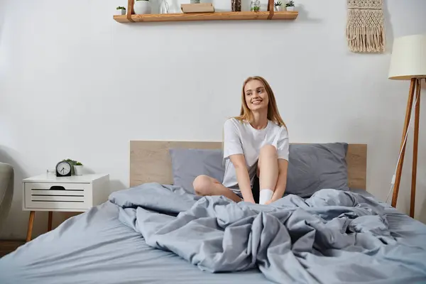 Una mujer joven se sienta en una cama en su dormitorio, disfrutando de un tiempo para sí misma. — Stock Photo