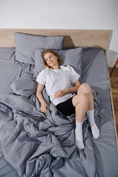 Una joven está acostada en la cama, sonriendo y mirando hacia arriba. - foto de stock