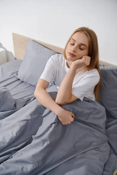 A young woman relaxes in bed, her eyes closed and her head resting on her hand. — Stock Photo