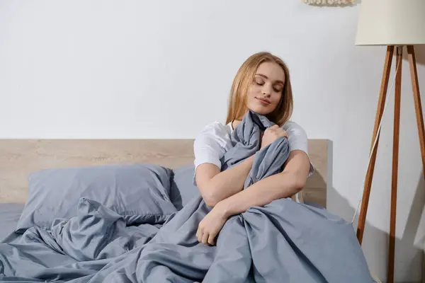 A young woman relaxes on her bed, wrapped in a grey blanket. — Stock Photo