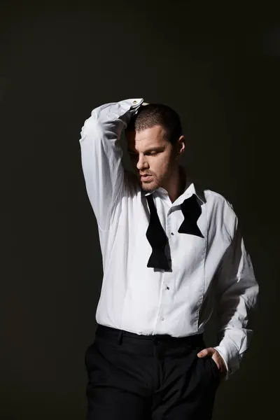 A man in a white shirt and black bow tie poses with his hand on his head. — Stock Photo