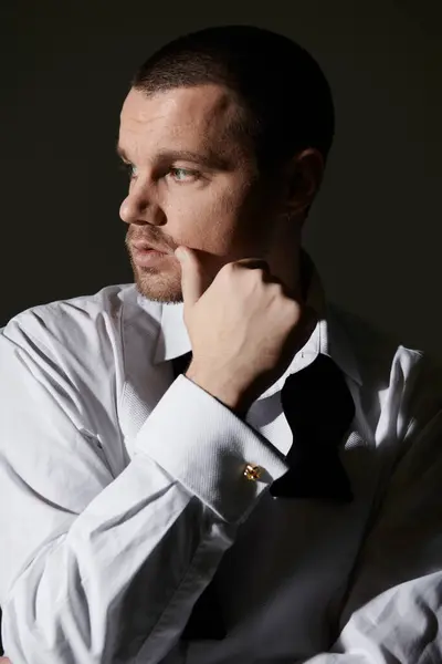 A stylish man in a white shirt and bow tie contemplates a thought, his hand resting on his chin. — Stock Photo