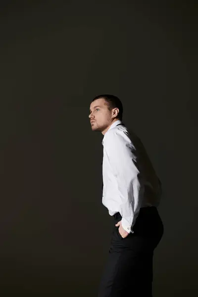 A man in a crisp white shirt and black trousers stands in a studio, gazing off to the side. — Stock Photo
