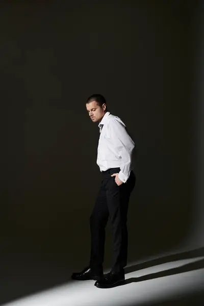 A man in a white shirt and black pants stands in a dark room, illuminated by a single spotlight. — Stock Photo