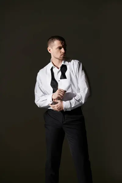 A man in a white shirt and black bow tie stands against a dark backdrop, adjusting his cufflinks. — Stock Photo