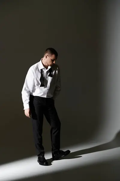 A man in a white shirt and black bow tie stands in a beam of light, looking down. — Stock Photo