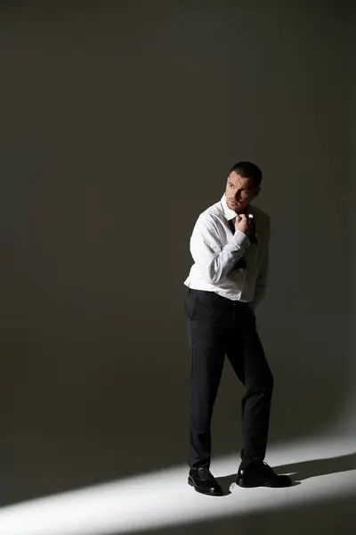A man in a white shirt and black trousers adjusts his tie in a dimly lit studio. — Stock Photo
