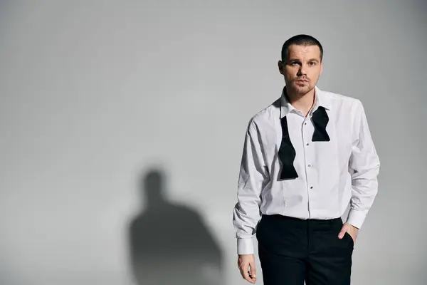 A man in a white shirt and black bowtie stands confidently against a light gray background. — Stock Photo