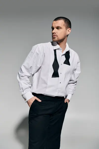 A man in a white shirt and a black bowtie stands with his hands in his pockets, looking to the side. — Stock Photo