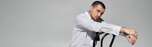 A man in a white shirt leans back on a chair, looking thoughtful and stylish. — Stock Photo