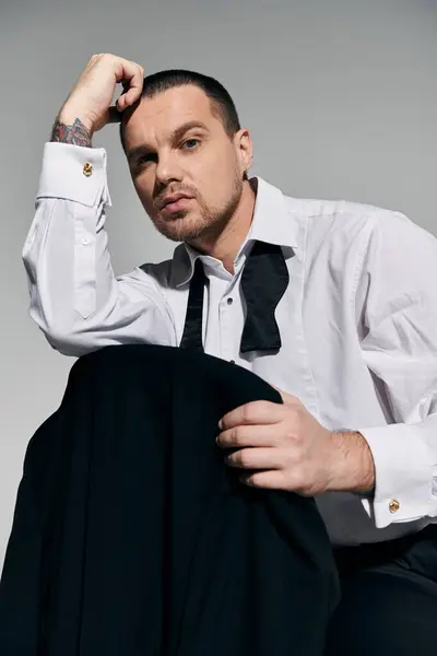 A stylish man with a black bowtie adjusts his white shirt, sitting against a plain backdrop. — Stock Photo