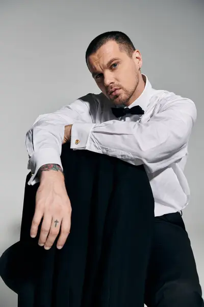A stylish man in a white shirt and a black bow tie sits, looking directly at the camera. — Stock Photo