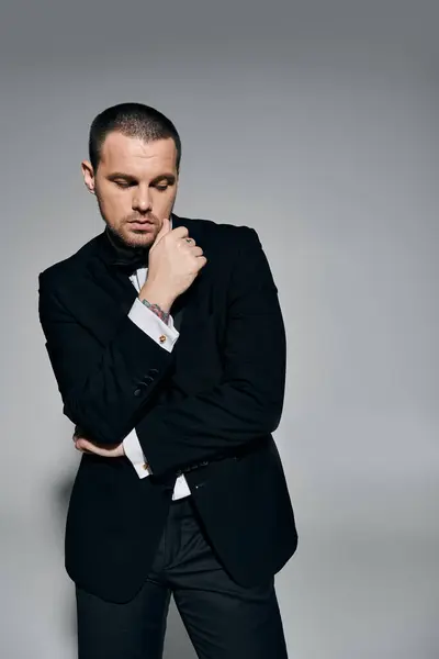 A man in a tuxedo stands in a studio, thoughtfully touching his chin. — Stock Photo