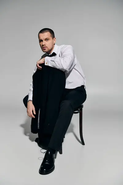 A man in a white shirt and black trousers sits on a stool, holding his jacket. — Stock Photo