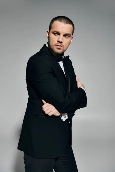 A man in a black tuxedo stands against a gray background, arms crossed, looking to the side. — Stock Photo