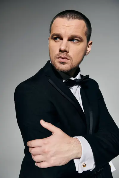 A stylish man in a black suit and bow tie stands against a grey backdrop. — Stock Photo