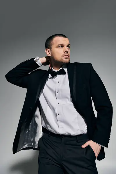 A man in a tuxedo stands against a gray background, his hand resting confidently on his hip. — Stock Photo