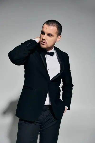 A man in a black tuxedo stands against a gray backdrop, adjusting his collar. — Stock Photo