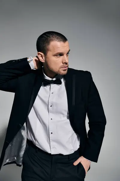 A man in a black suit and bow tie stands against a gray wall, adjusting his collar. — Stock Photo