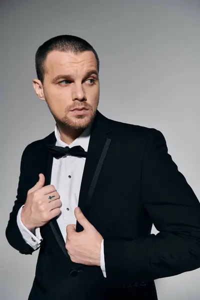 A man in a black suit and bow tie adjusts his jacket while looking off to the side. — Stock Photo
