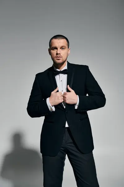 A man in a black tuxedo adjusts his bow tie with a confident and stylish pose. — Stock Photo