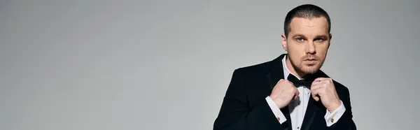 A man in a tuxedo adjusts his bow tie with a focused expression. — Stock Photo