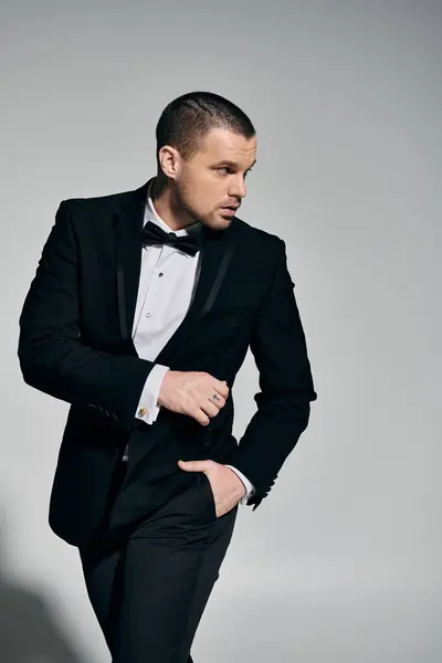 A man in a tuxedo stands confidently against a gray background. — Stock Photo