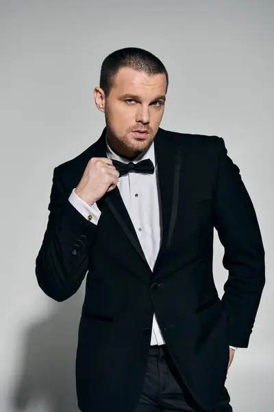 A man in a black tuxedo adjusts his bowtie, exuding confidence and style. — Stock Photo