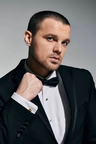 A man in a black tuxedo adjusts his bow tie with a confident gaze. — Stock Photo