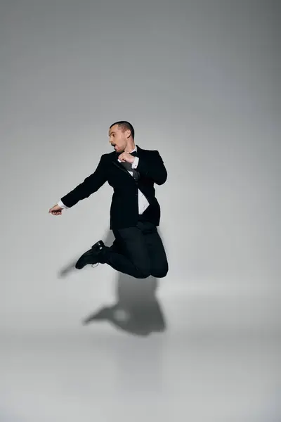 Um homem elegantemente vestido em um terno preto salta no ar, olhando por cima de seu ombro. — Fotografia de Stock