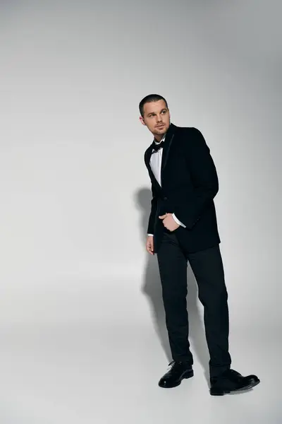 A man in a tuxedo stands against a white backdrop, looking to his left. — Stock Photo