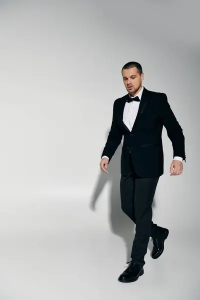 A dapper man in a black tuxedo walks confidently across a white studio floor. — Stock Photo