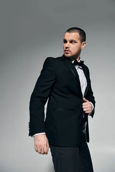 A man in a black tuxedo stands with his hand on his jacket, looking to the side. — Stock Photo