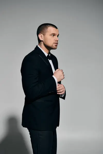 A man in a tuxedo adjusts his cufflinks against a gray backdrop. — Stock Photo