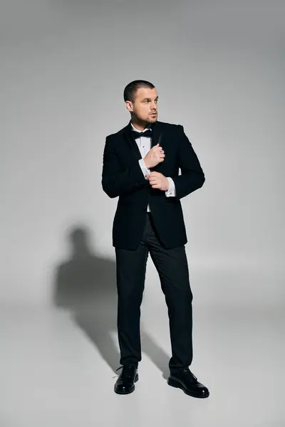 Man in tux adjusting cufflink against gray backdrop. — Stock Photo