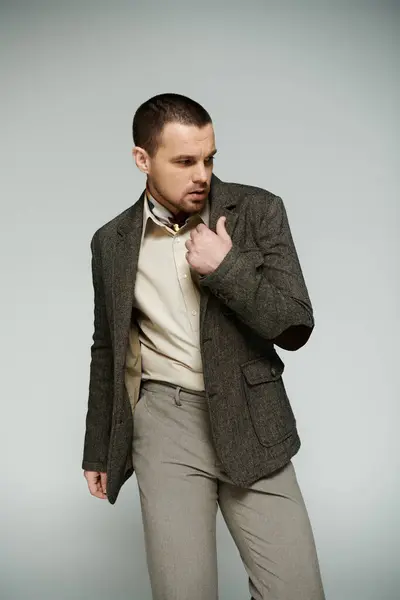 A stylish man in a tweed jacket stands against a gray backdrop, adjusting his collar. — Stock Photo