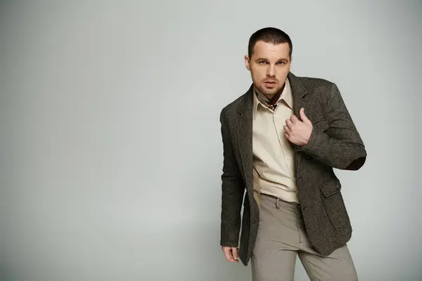 A stylish man in a tweed blazer and khaki pants poses against a grey background. — Stock Photo