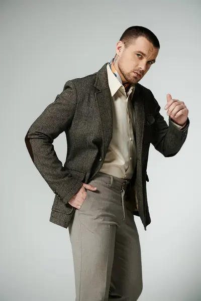 A stylish man in a tweed jacket and beige trousers poses against a light backdrop. — Stock Photo