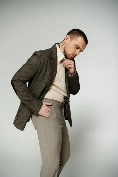 Man adjusts collar in tweed blazer and khakis against gray. — Fotografia de Stock