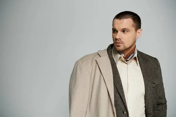 Un homme en manteau beige et un blazer à motifs regarde par-dessus son épaule avec une expression réfléchie. — Photo de stock