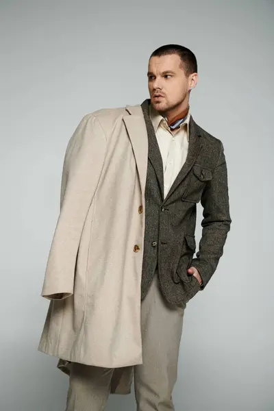 A man in a stylish brown jacket and a cream-colored coat, standing casually in a studio. — Stock Photo