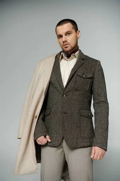 Un uomo in giacca di tweed e pantaloni beige si staglia su uno sfondo grigio. — Stock Photo