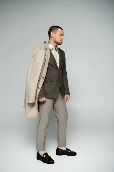 A stylish man poses in a studio, wearing a beige coat and a tweed blazer. — Stock Photo