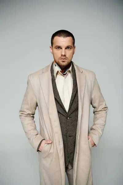 A stylishly dressed man in a tan coat and vest, standing with his hands in his pockets. — Stock Photo