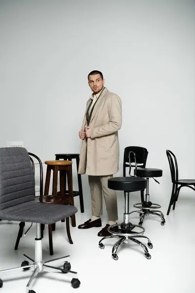 Un uomo sicuro trasuda eleganza senza tempo in una stanza con sedie variegate. — Foto stock