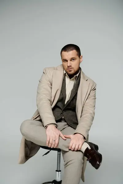 A man in a beige coat sits on a stool, his legs crossed. — Stock Photo