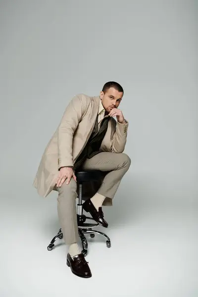 A man in a stylish beige suit sits on a chair, thoughtfully gazing at the camera. — Stock Photo