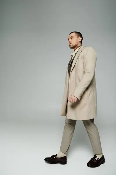 A stylish man in a beige trench coat walks confidently across a minimalist backdrop. — Stock Photo